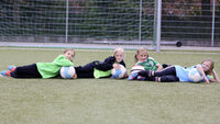 Vier Mädchen liegen auf dem Fußballplatz und posieren lächelnd mit ihren Trainingsbällen.