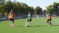 Junger Fußballer im Dribbling gegen zwei Gegenspieler während einer Trainingseinheit auf dem grünen Rasen.