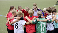 Kinderfußballteam steht im Kreis mit verschränkten Armen und motiviert sich gemeinsam vor dem Spiel.