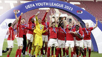 Jubelnde Jugendmannschaft in roten Trikots feiert unter dem „UEFA Youth League 2023“-Bogen, während ein Spieler den Pokal hochhält.