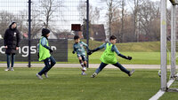 Ein Jugendfußballspieler schießt auf das Tor, während zwei Verteidiger versuchen, den Ball abzuwehren.