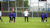 Trainer gibt Anweisungen während eines Jugendfußballtrainings auf einem Rasenplatz.
