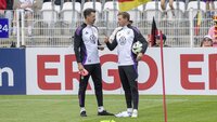 Zwei Fußballtrainer in Trainingskleidung des DFB stehen am Spielfeldrand und unterhalten sich.