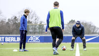 Trainer und Spieler beim Fußballtraining auf einem Kunstrasenplatz mit Fokus auf Ballkontrolle.