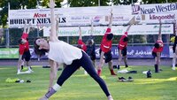 Fußballspieler machen Yoga-Übungen auf einem Sportplatz.