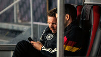 Ein Trainer der deutschen Nationalmannschaft sitzt auf der Bank und nutzt konzentriert sein Smartphone für die DFBnet Anmeldung.