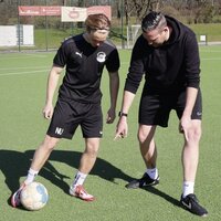 Zwei Personen auf einem Fußballplatz führen eine Übung mit einem Ball durch.