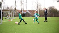 Zwei junge Fußballspieler in grüner Trainingskleidung spielen auf einem Rasenplatz mit einem Ball.