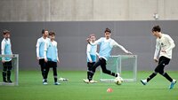 Jugendliche trainieren Fußball in einer Halle mit kleinen Toren und Leibchen.