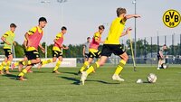 Spieler von Borussia Dortmund trainieren auf einem Fußballplatz mit Hütchen und Stangen.