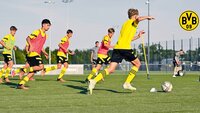 Spieler von Borussia Dortmund trainieren auf einem Fußballplatz mit Hütchen und Stangen.