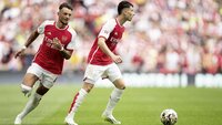 Zwei Spieler des FC Arsenal im rot-weißen Trikot laufen während eines Spiels über den grünen Rasen des Stadions.