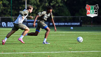 Zwei Fußballspieler sprinten auf einem Trainingsplatz einem rollenden Ball hinterher; beide in Trainingskleidung, im Hintergrund Tore und Bandenwerbung, rechts oben das NEC-Logo.
