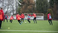 Jugendliche trainieren Fußball auf einem Kunstrasenplatz mit Leibchen in Teams aufgeteilt.