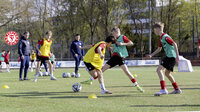 Jugendliche trainieren Fußball auf einem Rasenplatz mit Fortuna Köln-Logo im Hintergrund.