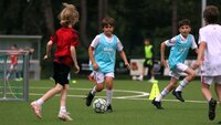 Kinder spielen Fußball auf einem Trainingsplatz mit Leibchen und Ball.