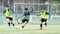 Fußballspieler in grünen Trikots trainieren auf einem Kunstrasenplatz mit Ball.