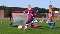 Kind schießt auf ein kleines Fußballtor, ein anderes Kind versucht zu verteidigen.