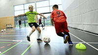 Kinder spielen Fußball in einer modernen Sporthalle mit Fokus auf Technik und Ballkontrolle.