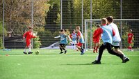 Kinder trainieren Fußballspiel auf einem Kunstrasenplatz mit Torübungen.