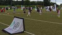 Viele Kinder und mehrere Trainer trainieren auf abgesteckten Feldern mit kleinen Toren und Hütchen auf einem Fußballplatz.