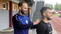 Eine Person passt einem Sportler eine Weste an, im Hintergrund ist eine Laufbahn und ein Stadion zu sehen.