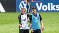 Ein Trainer gibt einem Spieler auf einem Fußballplatz Anweisungen und zeigt mit einem Stift auf etwas.