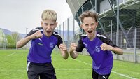 Zwei junge Fußballspieler in violetten Trikots posieren auf dem Spielfeld.