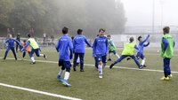 Fangspiel im Fußballtraining: Kinder in Leibchen jagen und weichen aus, Aktivierung auf Kunstrasen im Nebel