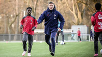 Trainer und Jugendspieler des 1. FC Köln laufen gemeinsam beim Fußballtraining auf dem Kunstrasenplatz.