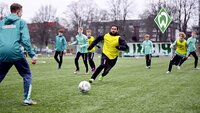 Spieler von Werder Bremen trainieren auf einem Fußballplatz mit Ball und Leibchen.