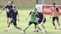 Die deutsche Nationalmannschaft trainiert auf dem Platz, wobei sich ein Spieler im grünen Leibchen gegen seine Mitspieler durchsetzt.