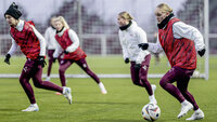 Frauenfußballteam trainiert im Winter auf Kunstrasen mit roten Leibchen und Ball.