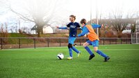 Zwei Kinder im Fußballtraining kämpfen um den Ball auf einem Kunstrasenplatz.
