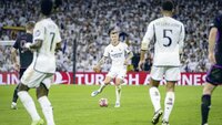 Toni Kroos von Real Madrid am Ball, umgeben von Bellingham und Vinicius Jr. in einem Champions League Spiel.