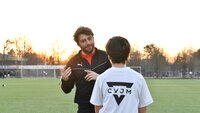 Ein Fußballtrainer gibt einem jungen Spieler vom CVJM auf dem Trainingsplatz im Sonnenuntergang wertvolle Tipps.