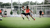 Zwei Fußballspieler im Zweikampf um den Ball während eines Trainingsspiels auf einem Rasenplatz.
