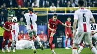 Ein Fußballspieler der Türkei schießt den Ball, während Gegenspieler in weißen Trikots versuchen, ihn zu blockieren.