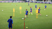 Jugendliche Fußballer der Red Bull Akademie trainieren Dribbling und Passspiel in einem Slalom-Parcours auf dem grünen Rasen.