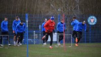 Spieler von Holstein Kiel absolvieren ein Athletiktraining mit Hürden und Stangen auf einem Trainingsplatz.