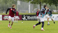 Fußballspieler trainieren auf einem regennassen Spielfeld, während ein Spieler mit Ballbesitz im Fokus steht.