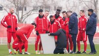 Eine Fußballmannschaft in roten Trainingsanzügen steht bei einer Taktikbesprechung auf dem Spielfeld.