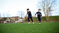 Zwei Kinder laufen während eines Fußballtrainings auf einem Kunstrasenplatz.