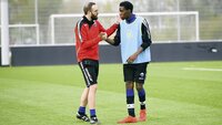 Ein Fußballtrainer spricht auf dem Trainingsplatz mit einem jungen Spieler und legt ihm die Hand auf die Schulter.