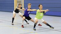 Drei Sportler machen Kniebeugen in einer Turnhalle.
