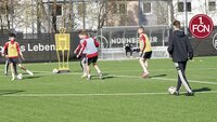 Spieler trainieren auf einem Fußballplatz mit kleinen Toren und Trainingsdummies.