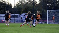 Fußballspielerinnen trainieren auf einem Feld mit einem Tor im Hintergrund.