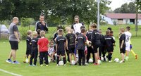 Eine Gruppe von Kindern und Trainern versammelt sich auf einem Fußballplatz für eine Besprechung.