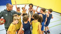Eine Kinder-Basketballmannschaft bildet einen Kreis und streckt die Hände in die Mitte.