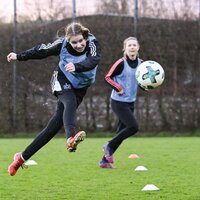 Eine Fußballspielerin führt auf einem Trainingsplatz einen Sprungstoß aus.